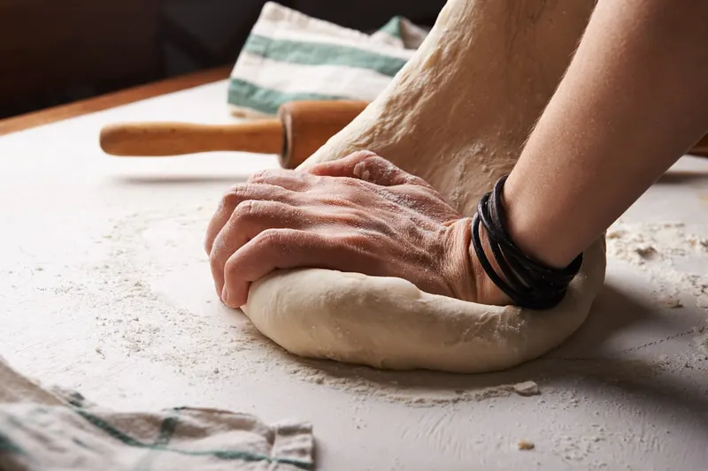 Mains pétrissant une pâte à pain sur un plan de travail fariné