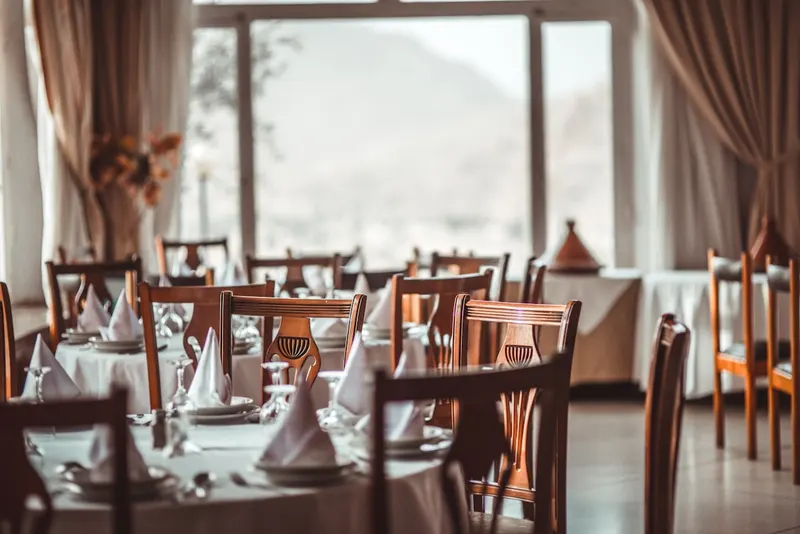 Salle du restaurant dressée, avec une grande fenêtre ouverte sur la montagne